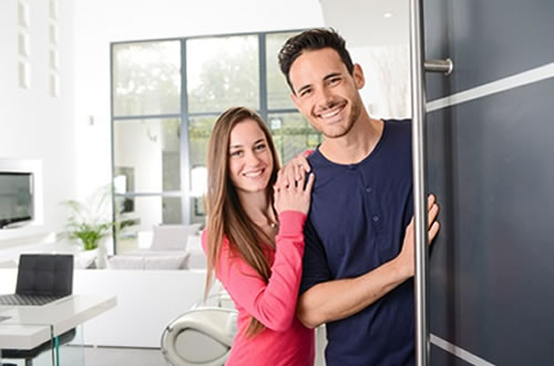 Junges Paar begrüßt Besucher an der Haustür